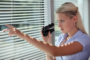 Woman spying through blinds holding binoculars