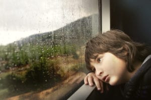 Young child looking out rain streaked window