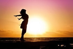 Woman pretending to fly in front of sunrise