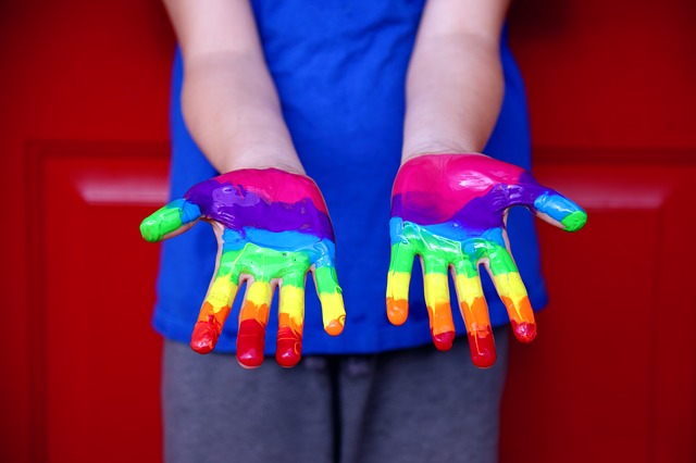 A young person's hands covered in rainbow colored paint, signifying gay pride.