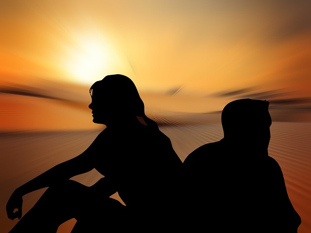 Silhouettes of a man and woman sitting back to back in front of a sunset.