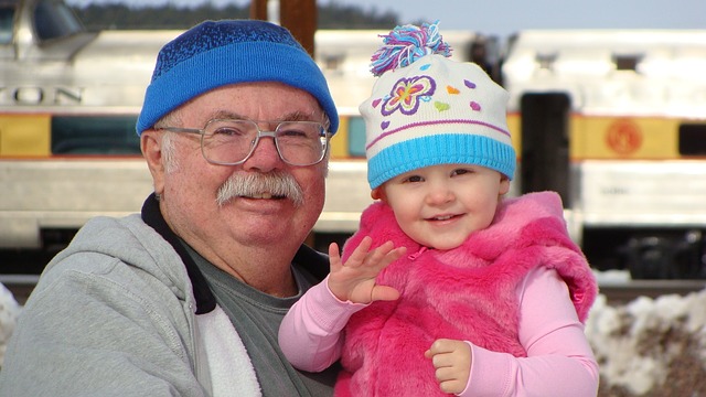 A grandfather and his granddaughter looking at the camera and waving. They're both smiling and look happy.