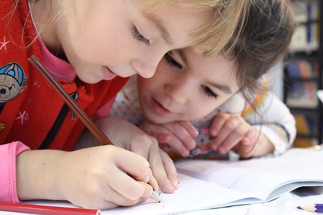 A close up picture of two little girls doing school work together at a table.